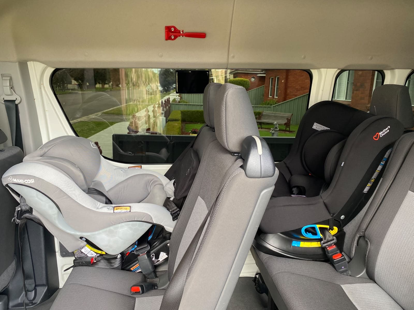 A grey infant capsule and a black rear-facing baby seat installed side by side in the middle row of our van