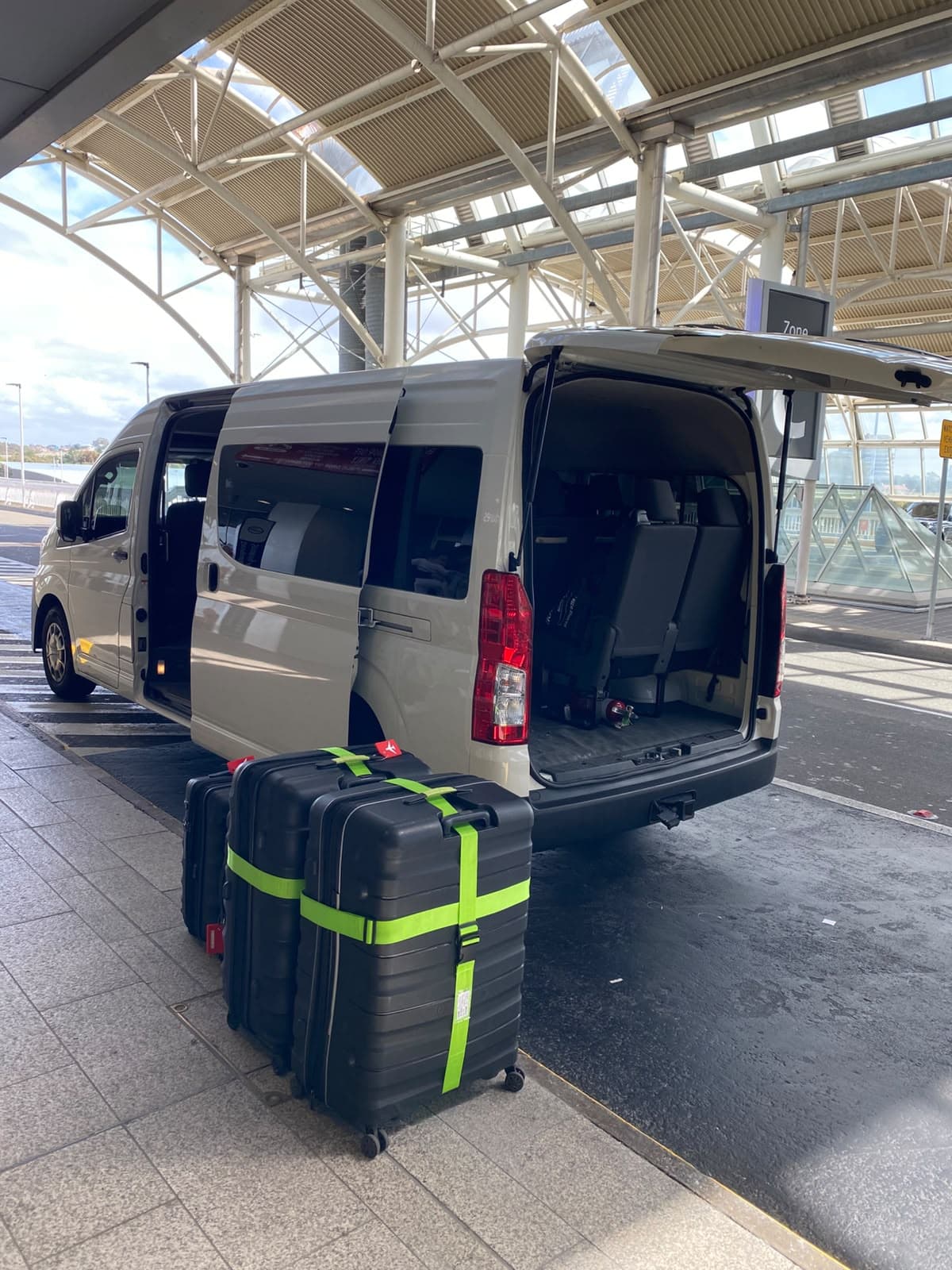 Our van waiting under the pick-up canopy at Sydney Airport, boot open, with four large suitcases on the kerb beside it
